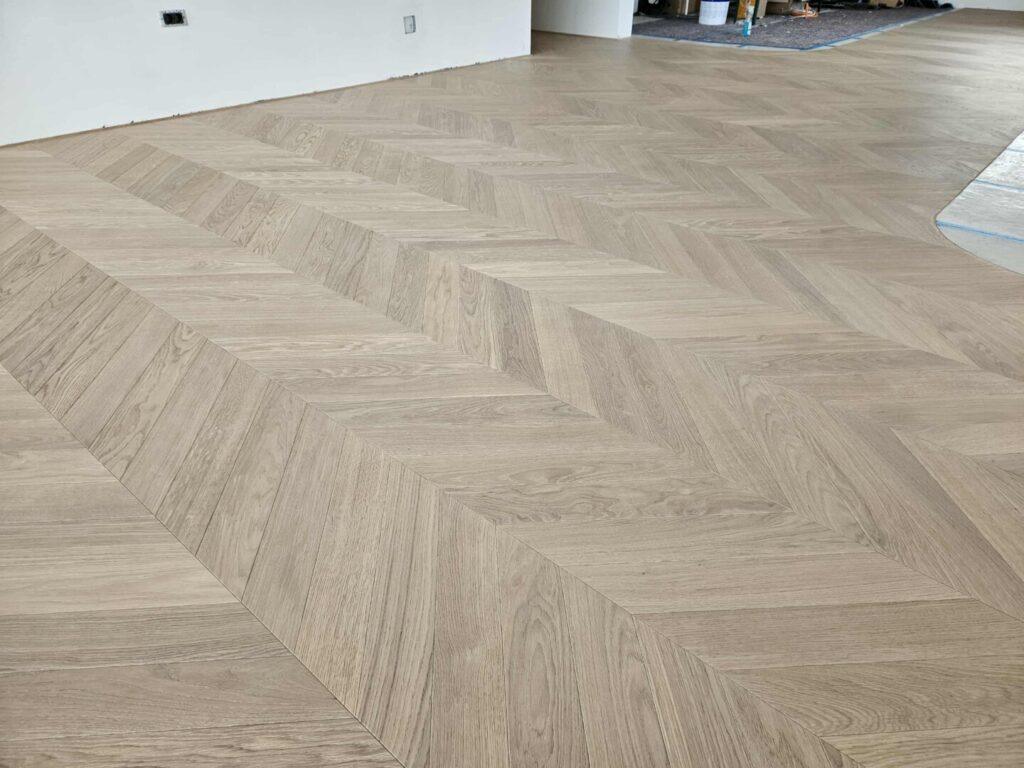 Skandinavski parket Hrast Natur MIST Chevron 45° v svetlem luksuznem interierju z geometrijskim vzorcem ribje kosti.
