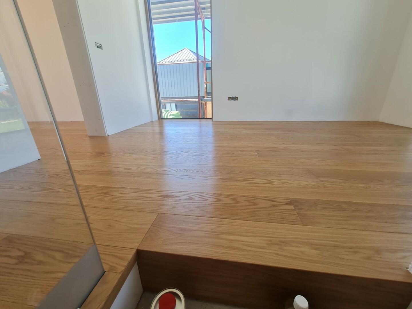 Detajl estetskega zaključka dvoslojnega hrastovega parketa ob odprtem balkonu v kombinaciji s stekleno ograjo v hiši v Domžalah.